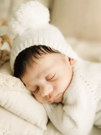 An intimate macro shot of the sleeping newborn, focusing on their delicate features and the texture of the pom-pom hat.