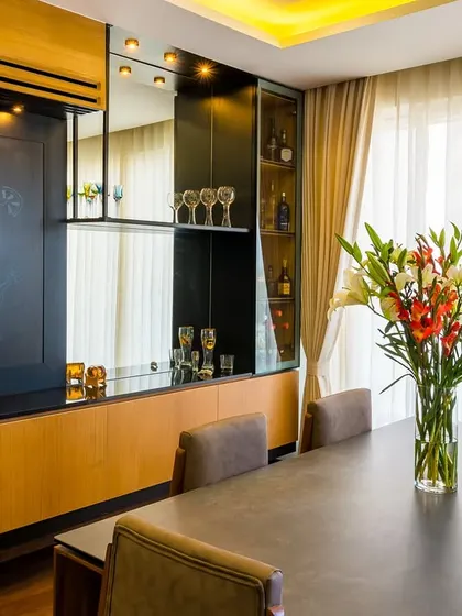 A sophisticated dining and bar area, perfect for entertaining. The design includes a built-in bar with glass storage, a chalkboard for a playful touch, and a large dining table, all unified by warm wood tones and ambient lighting.
