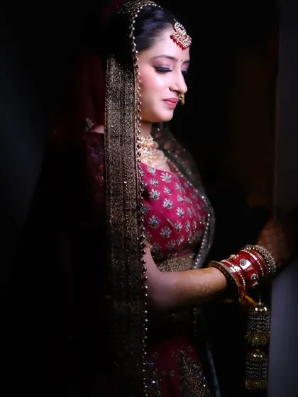 A classic bridal portrait, with the bride looking down, showcasing her intricate jewelry and the details of her veil.