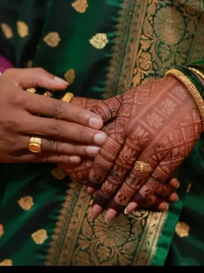 A close-up of the couple's hands, showing the intricate back-hand mehndi design. The dark stain looks beautiful against her traditional green saree.