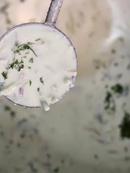 A ladle of our refreshing raita, showing the chopped vegetables mixed into the creamy yogurt.