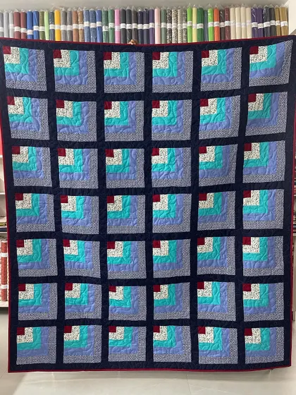 A "Quarter Log Cabin" quilt, where each block is built around a small red square. The cool blues and teals create a calming effect.