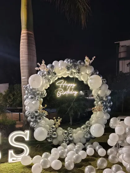 This elegant outdoor birthday decoration is perfect for evening parties. The combination of a chrome balloon wreath, a bright neon sign, and large marquee letters creates a stunning focal point on the lawn.