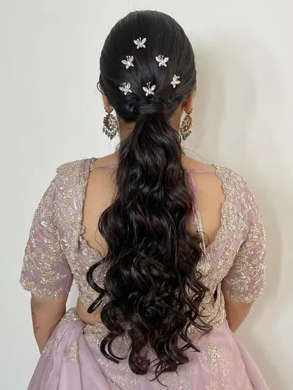 A modern and chic choice for a reception or sangeet. This long, wavy ponytail is adorned with delicate, butterfly-shaped pins, adding a touch of whimsy and glamour.