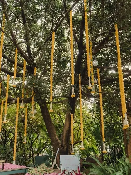 A tree at the venue decorated with hanging marigold garlands, integrating the natural landscape into the festive decor.