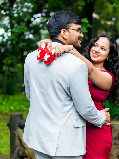 A playful and loving moment captured from behind. The mother-to-be drapes the baby shoes over her partner's shoulder, creating a unique and charming composition for their maternity shoot.
