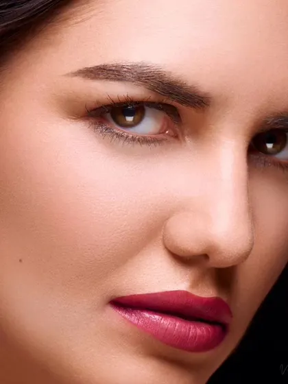 An extreme close-up beauty shot. The lighting is carefully controlled to highlight the flawless skin texture and the rich color of the lipstick, demonstrating technical skill in macro beauty photography.