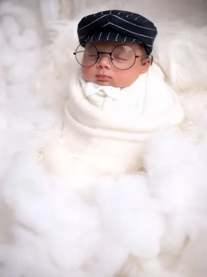 Adding a touch of personality with a little bow tie and glasses, this baby looks like a tiny scholar sleeping on a fluffy cloud.