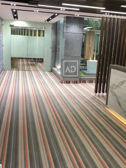 For this modern office lobby, I used striped wall-to-wall carpet to create a sense of direction and space. This type of commercial carpeting is designed for high foot traffic and provides sound insulation, which is essential in a busy work environment.
