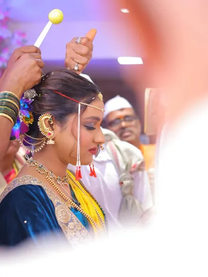 A candid moment from a Maharashtrian wedding ceremony. The bride's makeup is designed to look beautiful from every angle, even during rituals.