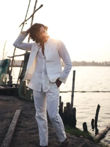 A full-length shot of the white-on-white premiere look, set against a serene backwater location in Kerala.