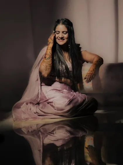 A graceful bride sitting with her mehandi-adorned hands. The reflection on the floor adds a touch of magic to the picture.