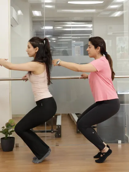 A close-up of a plié squat at the barre, a fundamental move that strengthens the entire lower body.