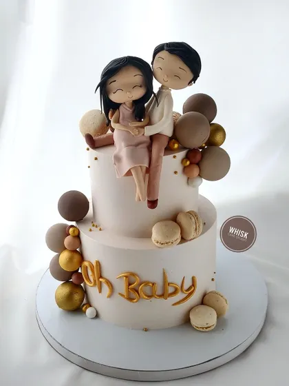 A beautiful baby shower cake for a growing family. This two-tiered cake features a handcrafted figurine of the expecting couple, surrounded by earthy-toned macarons and balloons.