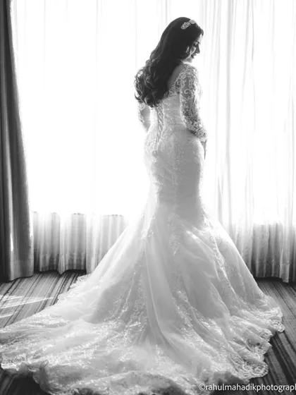 A classic black and white bridal portrait, showcasing the elegant silhouette and long train of her wedding gown.