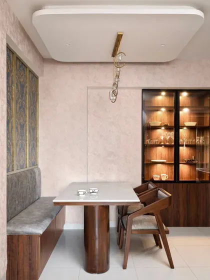 The dining area in the 'Muditā' home features a custom bench seater and a marble-top table. A lit bar and crockery unit with glass doors provides a beautiful display and separates the space from the kitchen.