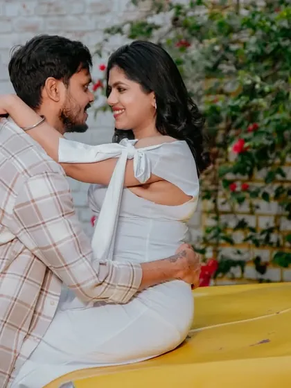A romantic and playful moment with the mother-to-be sitting on the hood of a vintage car, embracing her partner.