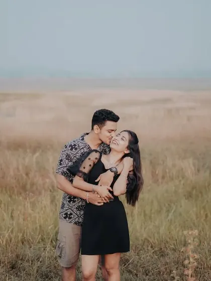 A happy and candid moment in a field of tall grass, with the groom whispering to the bride.