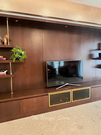 A detailed view of the custom-designed TV unit in an Indian contemporary home. The unit features a rich wood finish and open shelves supported by sleek metal rods, providing ample space for decor and media equipment.