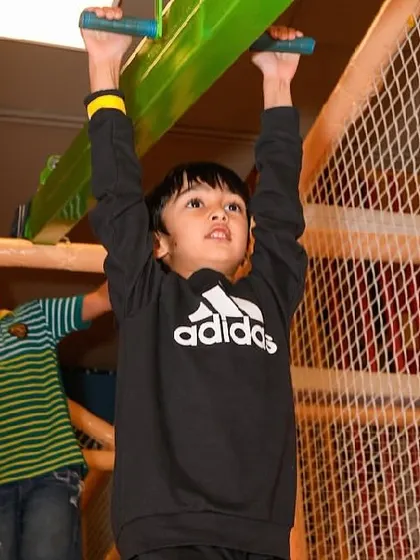 A boy tests his strength and coordination on the monkey bars inside our play structure.