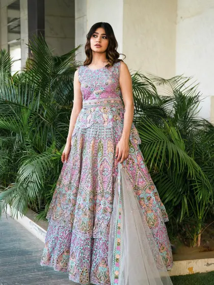 An ivory peplum achkan lehenga with intricate, multi-colored cut work and hand embroidery. This unique silhouette is a modern take on traditional wear, perfect for a fashion-forward wedding guest.