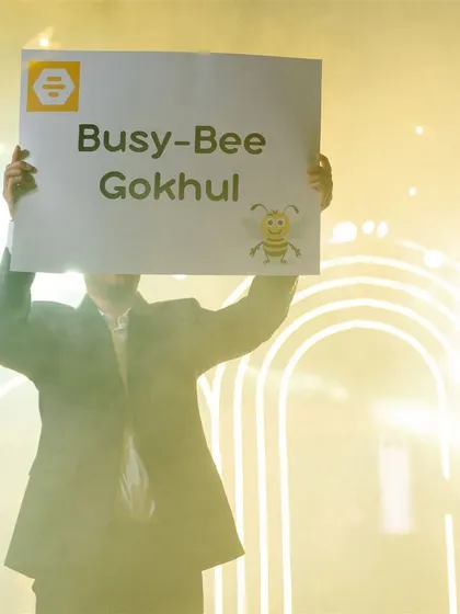 A friend holds up a "Busy-Bee Gokhul" sign, a fun and personal prop used to tell the couple's story.
