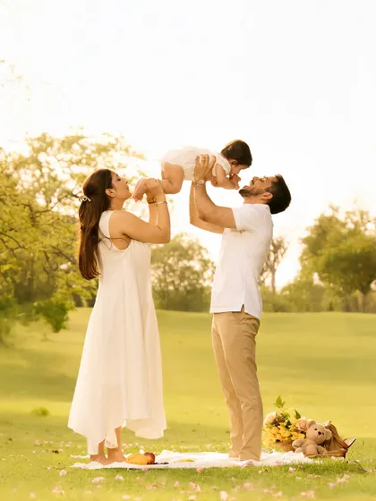 A father lifts his child towards the sun in a beautiful park, creating a classic, joyful pose that symbolizes love and aspiration. The warm, natural light enhances the emotional feel of the photo.