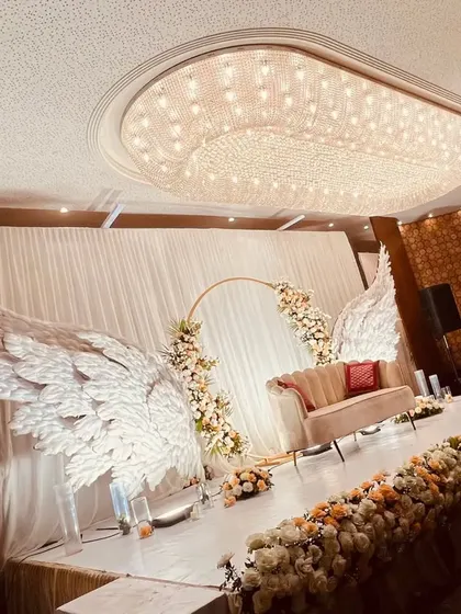A truly angelic stage design featuring magnificent white wings flanking a central floral ring. This unique and ethereal concept creates a heavenly photo opportunity and a memorable focal point for the event.