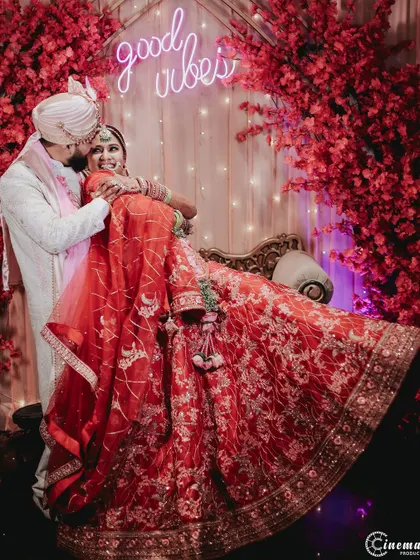 A fun and playful moment between the couple, captured against a vibrant red floral backdrop with a "good vibes" neon sign.