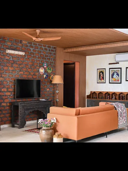 A wide view of the family lounge in our "Colors of Goa" project, showing how the rustic brick wall, wooden ceiling, and bespoke bar unit come together to create an earthy and stylish space.