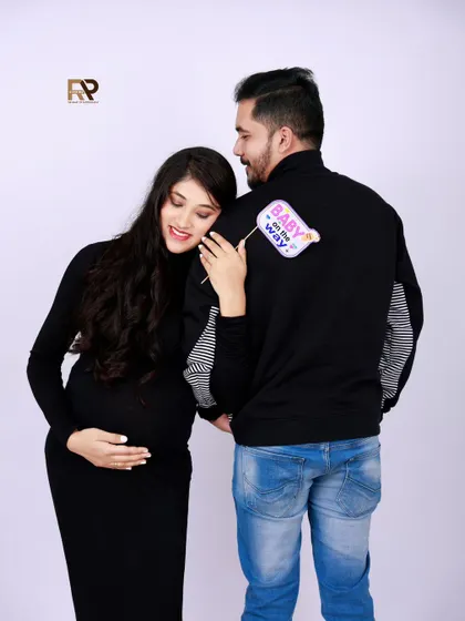 A playful and cute announcement. The mom-to-be holds a "Baby on the way" sign, leaning against her partner in this sweet and modern couple's shot.
