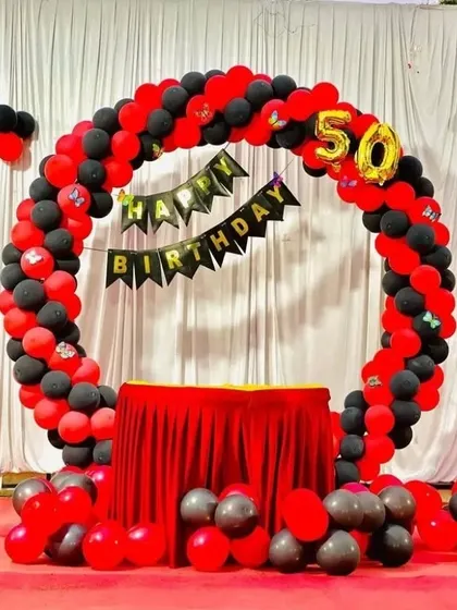 A bold red and black theme for a 50th birthday. This circular balloon arch frames a cake table, with a 'Happy Birthday' banner and a foil number '50' marking the milestone.