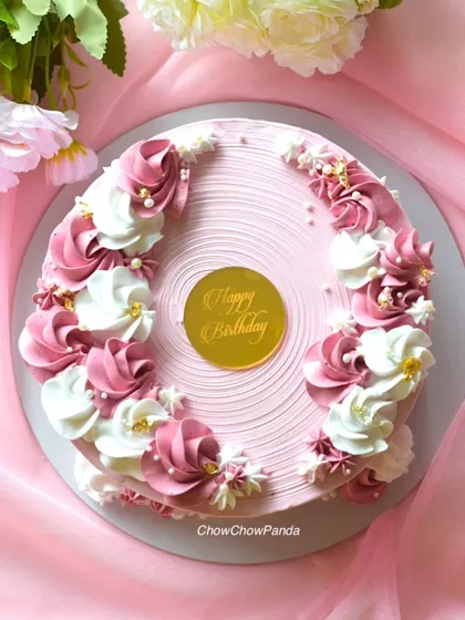 A top-down view of a floral cake with pink and white buttercream rosettes. This vanilla cake has a lovely textured finish and is dotted with small edible pearls.