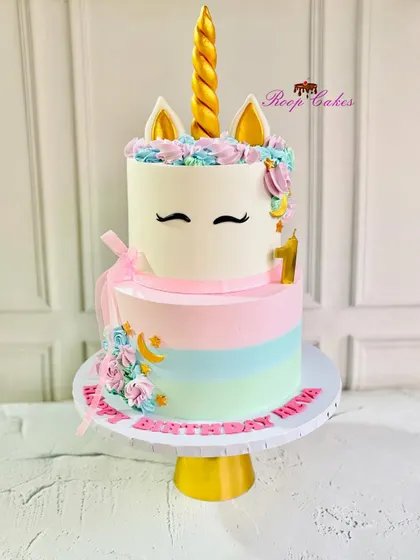 A dreamy unicorn delight to celebrate a big first birthday. This two-tier cake features pastel rainbow stripes on the bottom and a cute unicorn face on top, complete with a golden horn.
