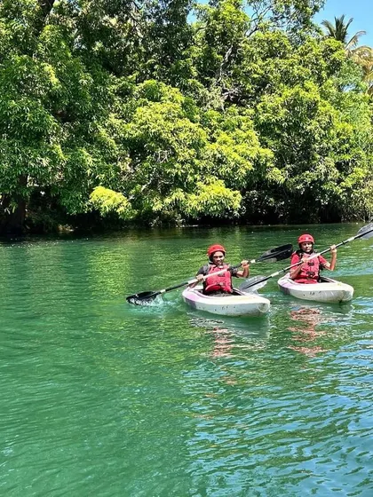 Two kayakers paddle in sync, exploring the lush riverbanks of Dandeli during a summer camp session.