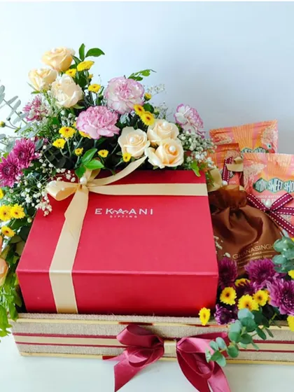 A vibrant and celebratory invitation hamper featuring a large red gift box from Ekaani. I surrounded it with a colorful array of fresh flowers and other treats to create a truly joyful and abundant presentation.