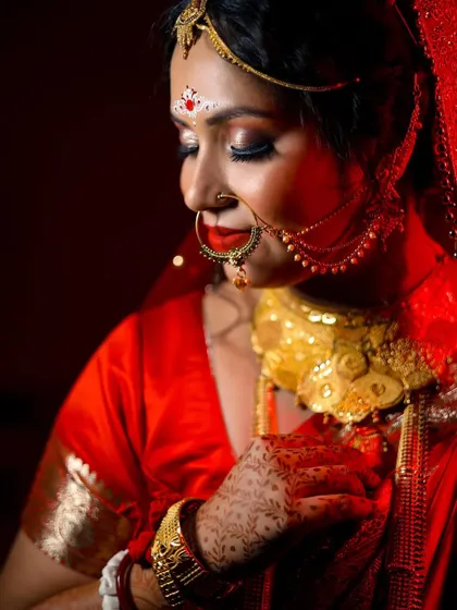 A classic and elegant portrait of the Bengali bride. The soft lighting and her graceful pose highlight the rich details of her saree and gold jewelry.