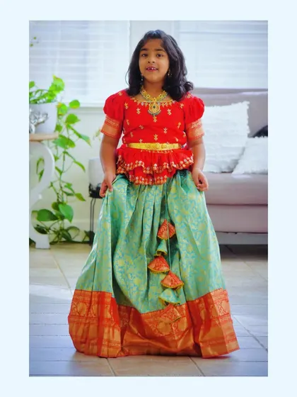 Our client from the USA looks gorgeous in her turquoise Kanchi pattu lehenga. The red maggam work blouse adds a pop of color, and the traditional gold border gives it a festive finish.