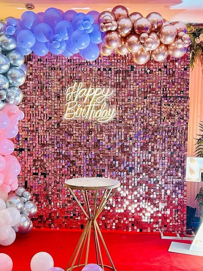 A colorful 75th birthday backdrop with a rose gold shimmer wall. The balloon arch uses a mix of pastel colors, and the setup includes large marquee numbers.