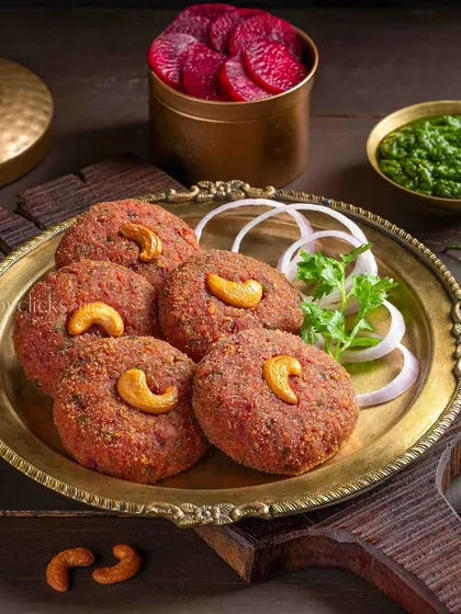 Beetroot and cashew tikkis, served on a traditional brass plate with onion rings and mint chutney.