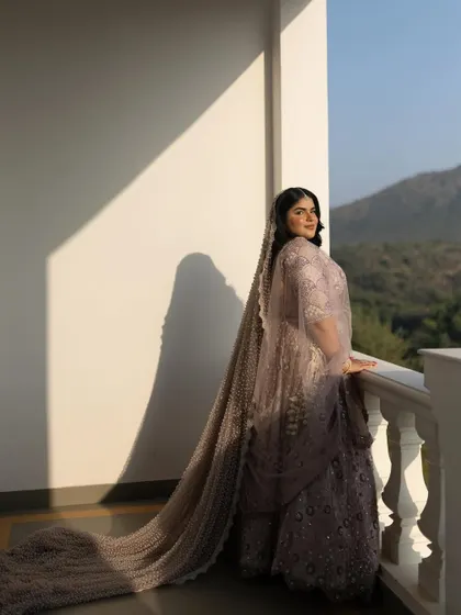 The bride stands on a balcony, with the morning sun casting a dramatic shadow against the wall, creating a powerful and artistic portrait.