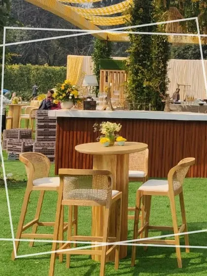 A high-top table and chair setup in the garden, perfect for a relaxed conversation. The natural wood furniture and the surrounding greenery create a simple and elegant look.