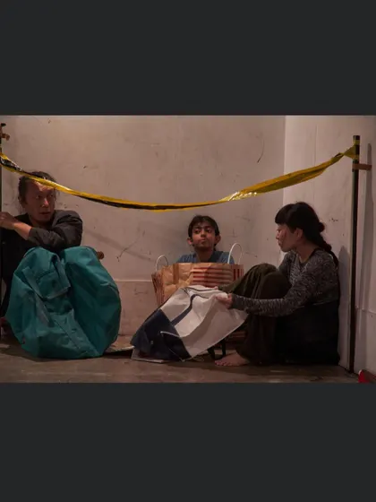 A still from a theatre piece, showing performers huddled together. This image powerfully conveys a sense of displacement and vulnerability, themes I often explore in my collaborative work.