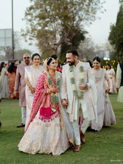 The couple walks hand-in-hand after their wedding ceremony, surrounded by their family. This photo captures a candid moment of togetherness and the beginning of their new journey.