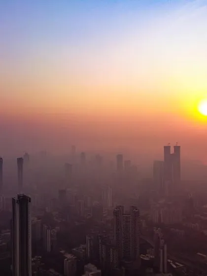 A high-altitude drone shot of the sun setting over a smog-filled Mumbai, creating a scene reminiscent of Delhi's hazy winters.