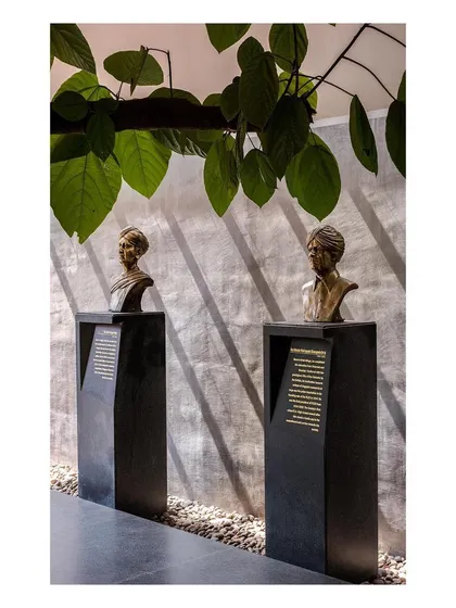 Detail of the founder busts in the Rishi Pavilion. The interplay of natural light filtering through the trees and the solid presence of the stone pedestals is a key part of the design.