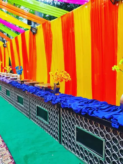 For this outdoor party, I set up a long buffet counter. The counter is decorated with blue fabric, and the backdrop features bright, colorful drapes that match the event's theme.