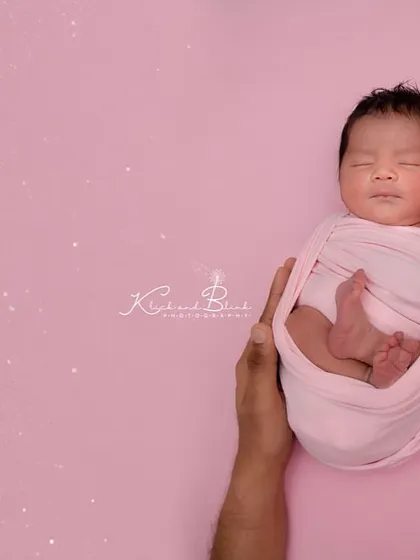 Held safely in her parents' hands. This shot focuses on the tiny, swaddled baby against a clean pink background, emphasizing how small and protected she is.