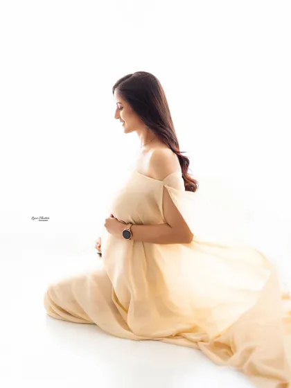 A quiet, contemplative profile shot. The soft, flowing fabric of the gown and the simple white background create a peaceful and elegant image, focusing on the beautiful silhouette.