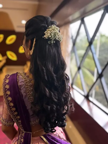 A closer look at the half-up hairstyle, showing the placement of the baby's breath and the texture of the curls. This is a perfect style for a half-saree function.